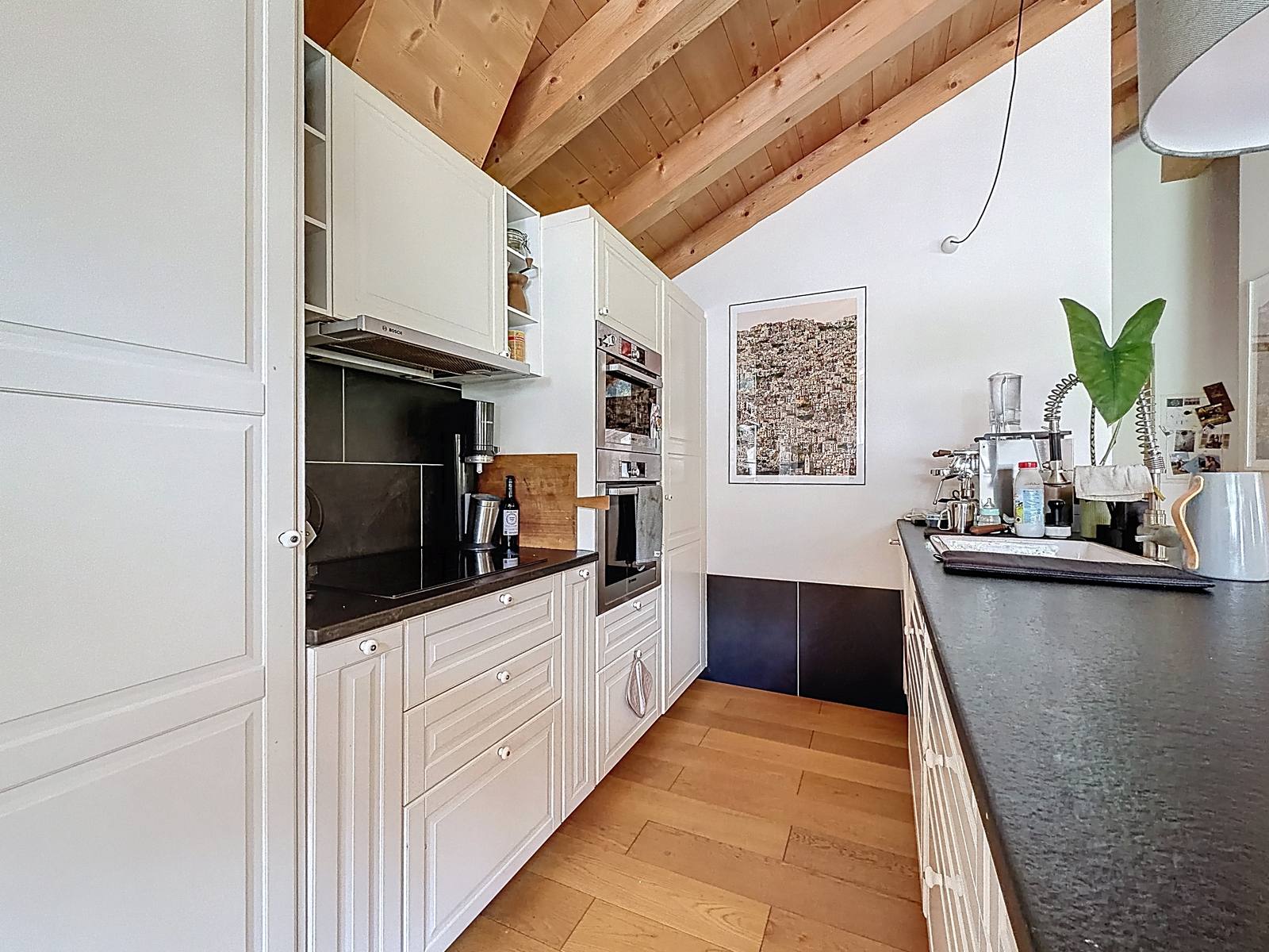 La cuisine équipée : four, plaques, colonnes de rangement et plan en pierre.