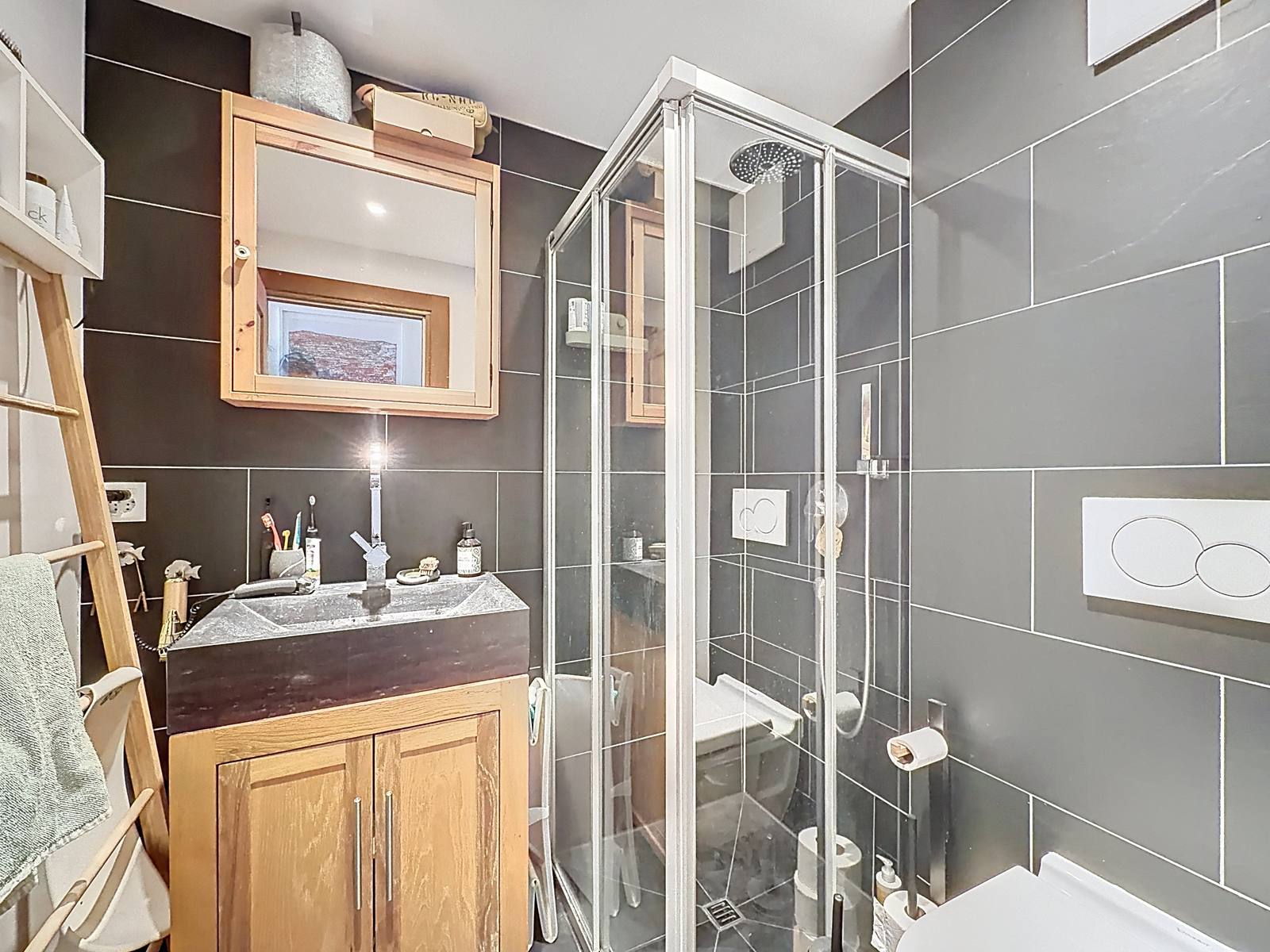 La salle de douche avec cabine vitrée, meuble vasque en bois et WC.
