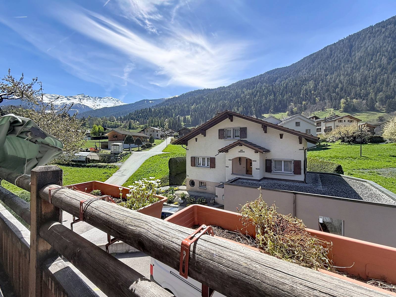 Vue depuis le balcon vers les prés, les chalets voisins et les sommets enneigés.
